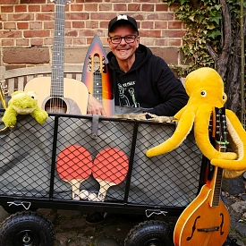 Herr Müller und seine Gitarre mit einem Bollerwagen voller Instrumente und Kuscheltiere